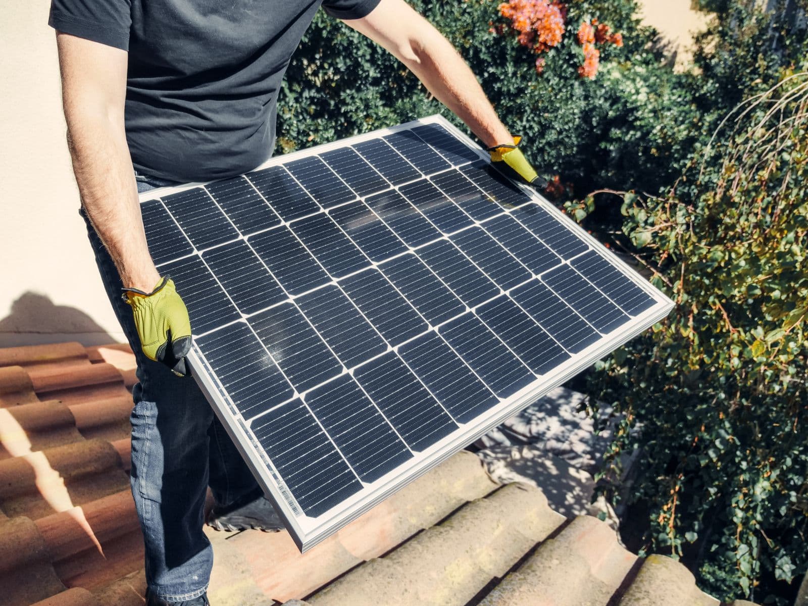 Installer carrying a solar panel across a terracotta tile roof